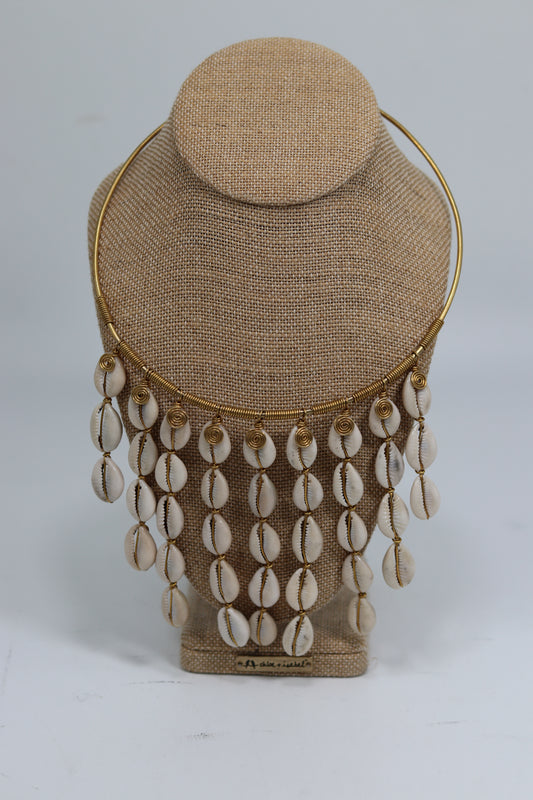 Handmade Kenyan brass choker necklace displayed on a beige burlap bust, featuring a gold-tone wire-wrapped collar adorned with a rich cascading fringe of natural white cowrie shells