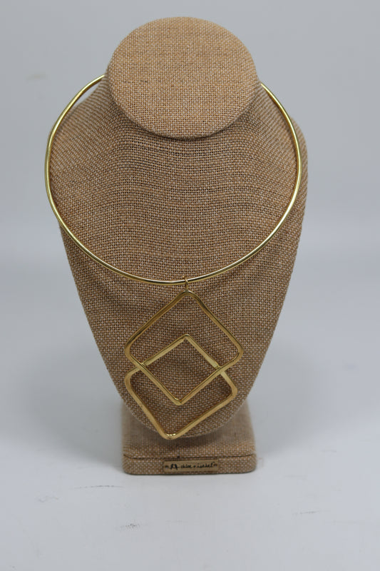 Handmade Kenyan brass choker necklace displayed on a beige burlap bust, featuring a smooth gold-tone collar wire and an architectural drop pendant composed of two overlapping geometric square frames.