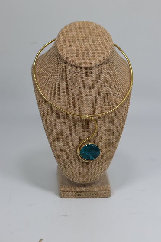 Handmade Kenyan brass choker necklace displayed on a beige burlap bust, featuring a smooth gold-tone collar wire and an elegant S-curve drop pendant holding a polished dark blue stone.