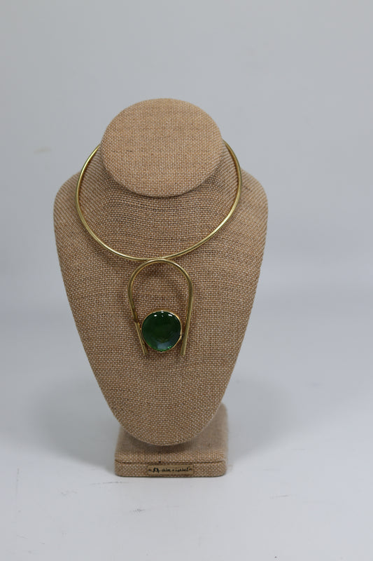Handmade Kenyan brass choker necklace displayed on a beige burlap bust, featuring a smooth gold-tone collar wire and an inverted U-shaped drop pendant holding a polished rich green round stone.
