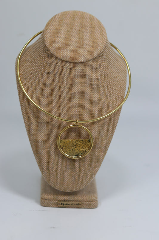 Handmade Kenyan brass choker necklace featuring a smooth rigid collar and an open circular pendant with a textured half-moon inlay, displayed on a burlap jewelry bust.