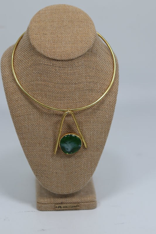 Handmade Kenyan brass choker necklace with a rigid collar and an open triangle drop pendant holding a round green stone, displayed on a burlap jewelry bust.