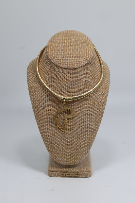Handmade Kenyan brass choker necklace displayed on a beige burlap bust, featuring a textured hammered gold-tone collar wire and a dangling cut-out brass pendant in the shape of the African continent.
