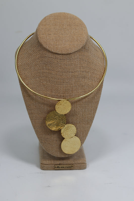 Hand-hammered Kenyan brass choker necklace displayed on a beige burlap bust, featuring a smooth gold-tone neck collar with four asymmetrical cascading textured round brass discs.
